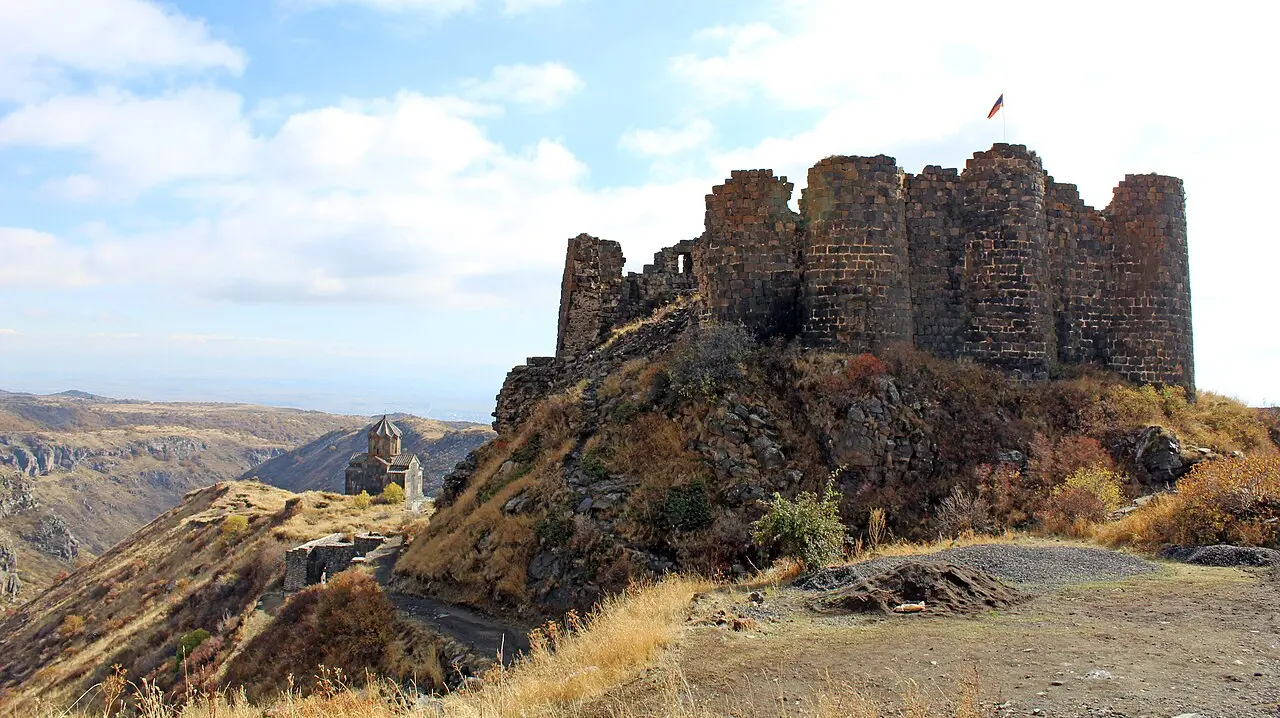 Amberd fortress and the Vahramashen church on a spur of Mount Aragats above a deep gorge, an Armenian flag flying over the walls under an autumn sky