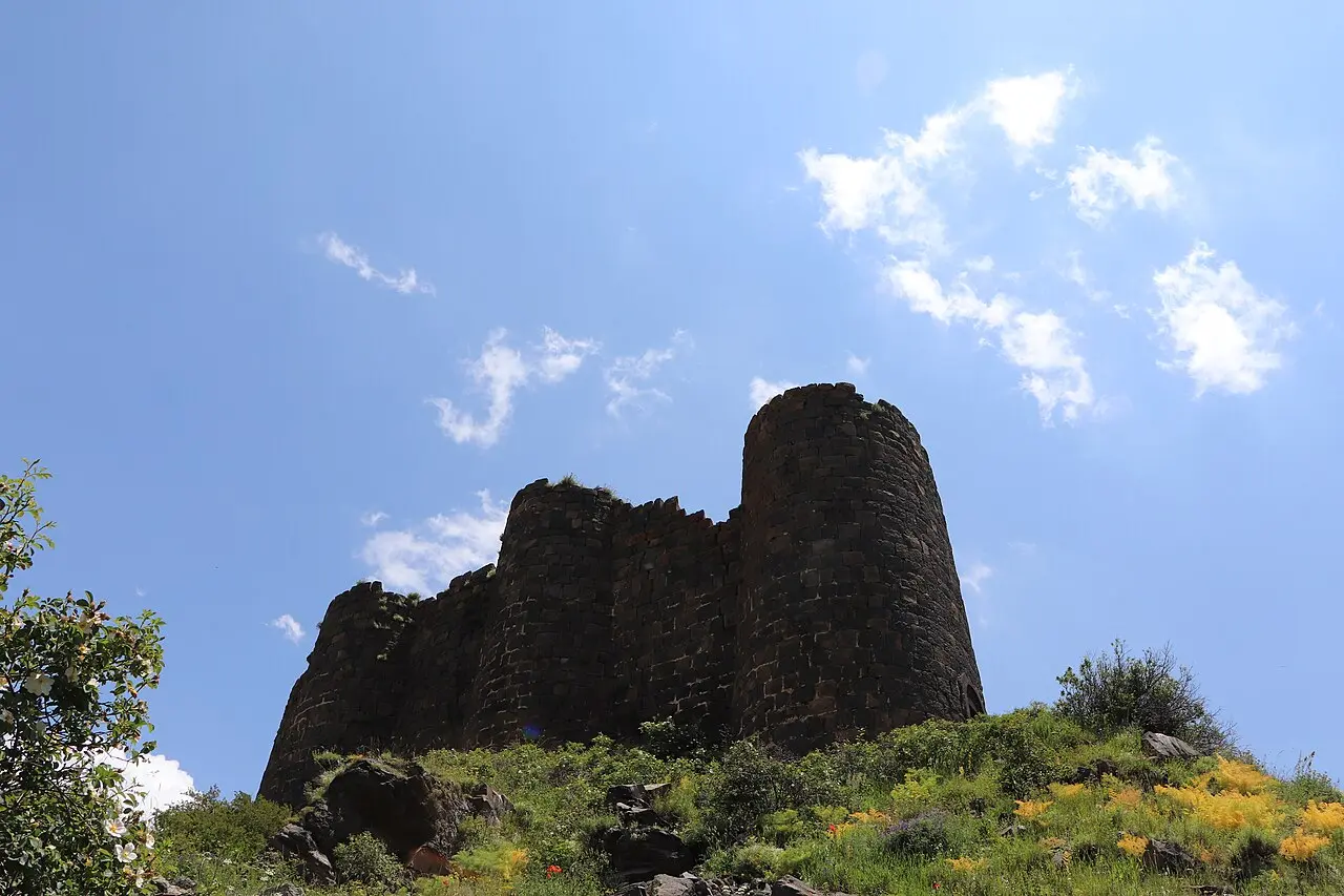 A single round tower of Amberd fortress silhouetted against a bright blue sky streaked with cloud