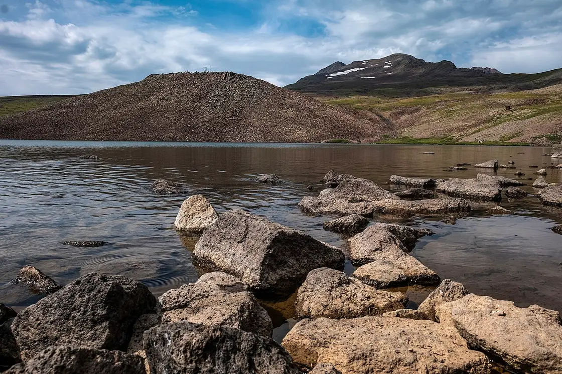 The still water of Lake Kari on the high slopes of Mount Aragats with snow patches on the peaks