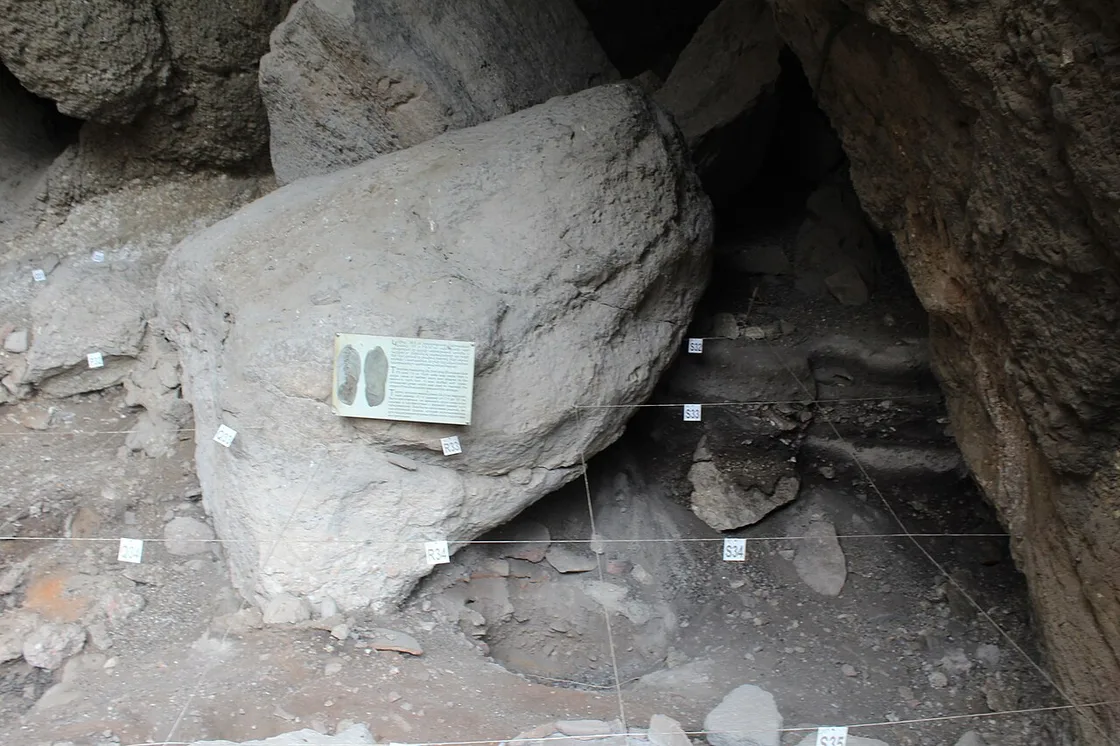 The excavation floor inside Areni-1 cave, marked out with a numbered survey grid and an information panel on a boulder