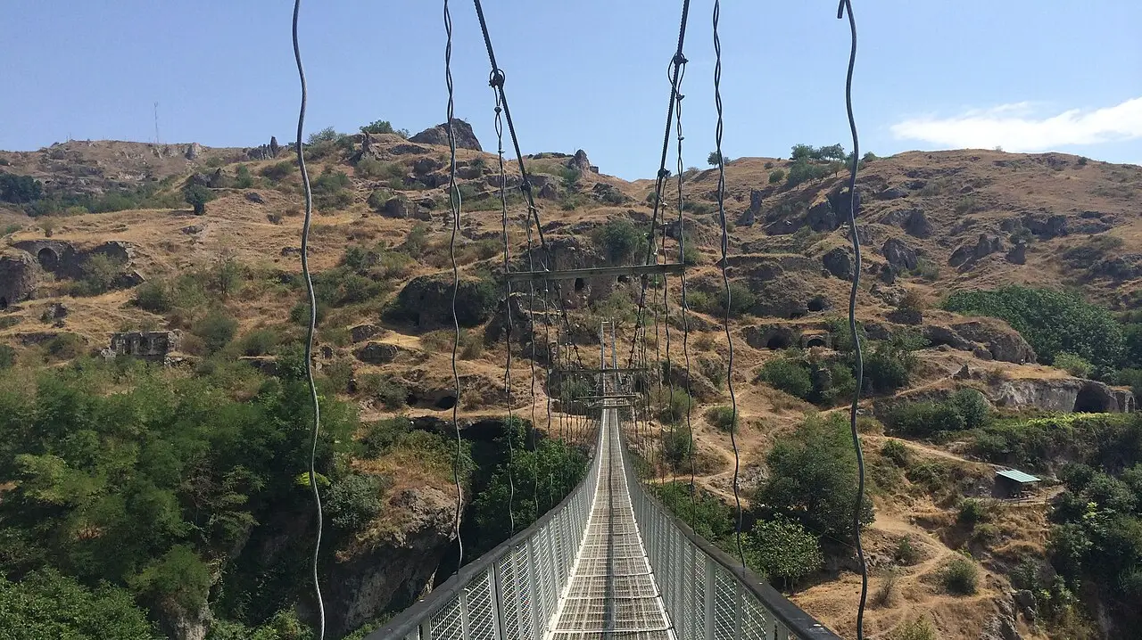 The long metal swinging bridge of Khndzoresk stretching across a gorge dotted with old cave dwellings in southern Armenia
