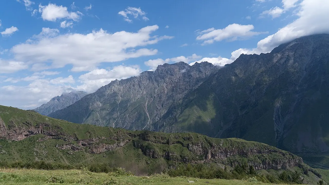 A sweeping view of the green slopes and craggy peaks of the Greater Caucasus near Gergeti in northern Georgia under a blue summer sky