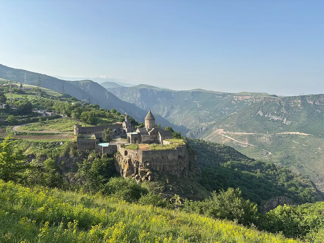 Tatev monastery on a green promontory above a deep gorge in southern Armenia, with mountains fading into the distance