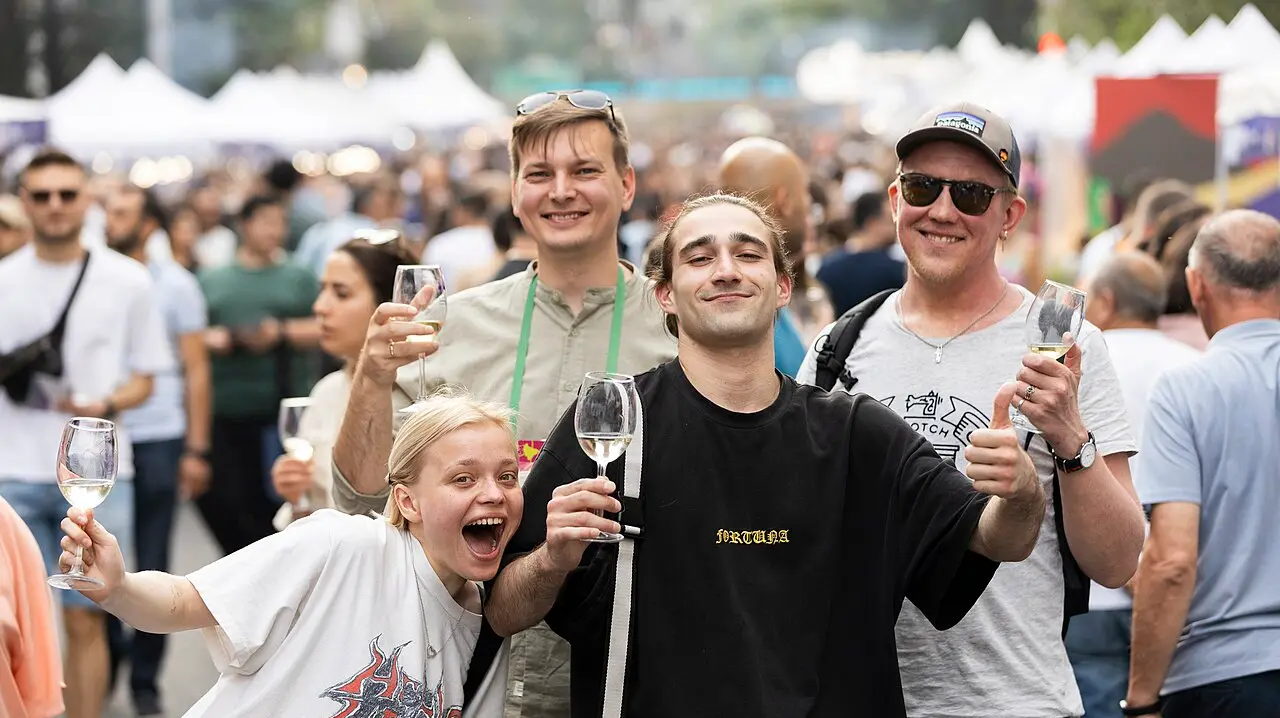 Smiling visitors holding glasses of wine in a crowded street at the Yerevan Wine Days festival