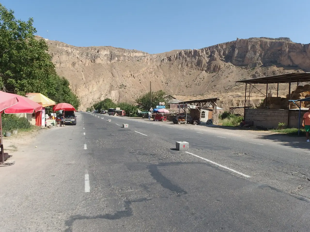 Roadside stalls with red umbrellas along the M2 highway at Areni under pale rock cliffs
