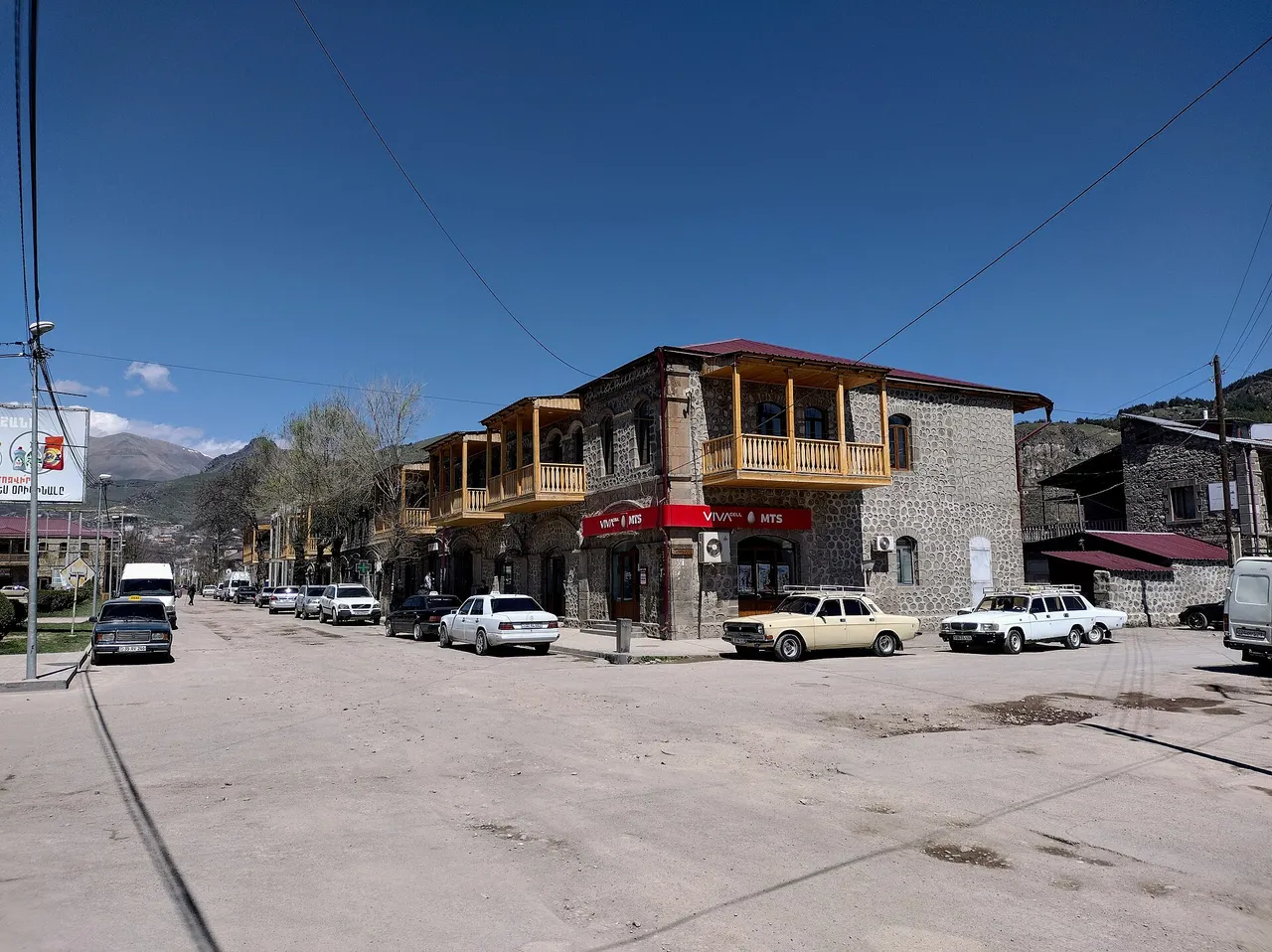 A street corner in Goris with an old stone house with wooden balconies and parked cars
