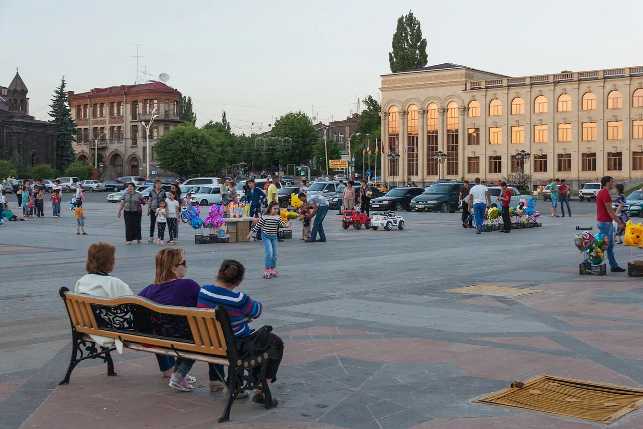 People sitting on benches on Vardanants Square in Gyumri with tuff buildings behind