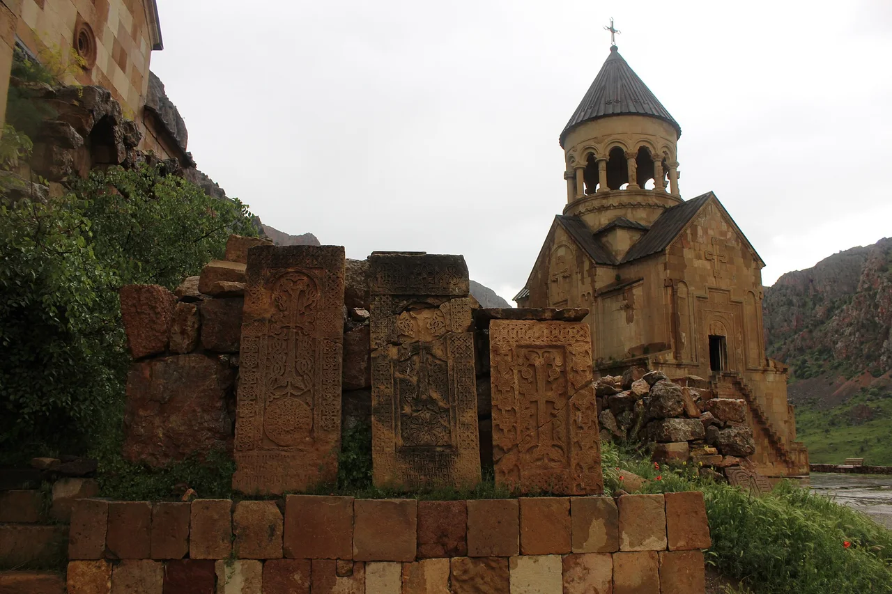 The domed church of Noravank behind a row of carved khachkars with red cliffs beyond