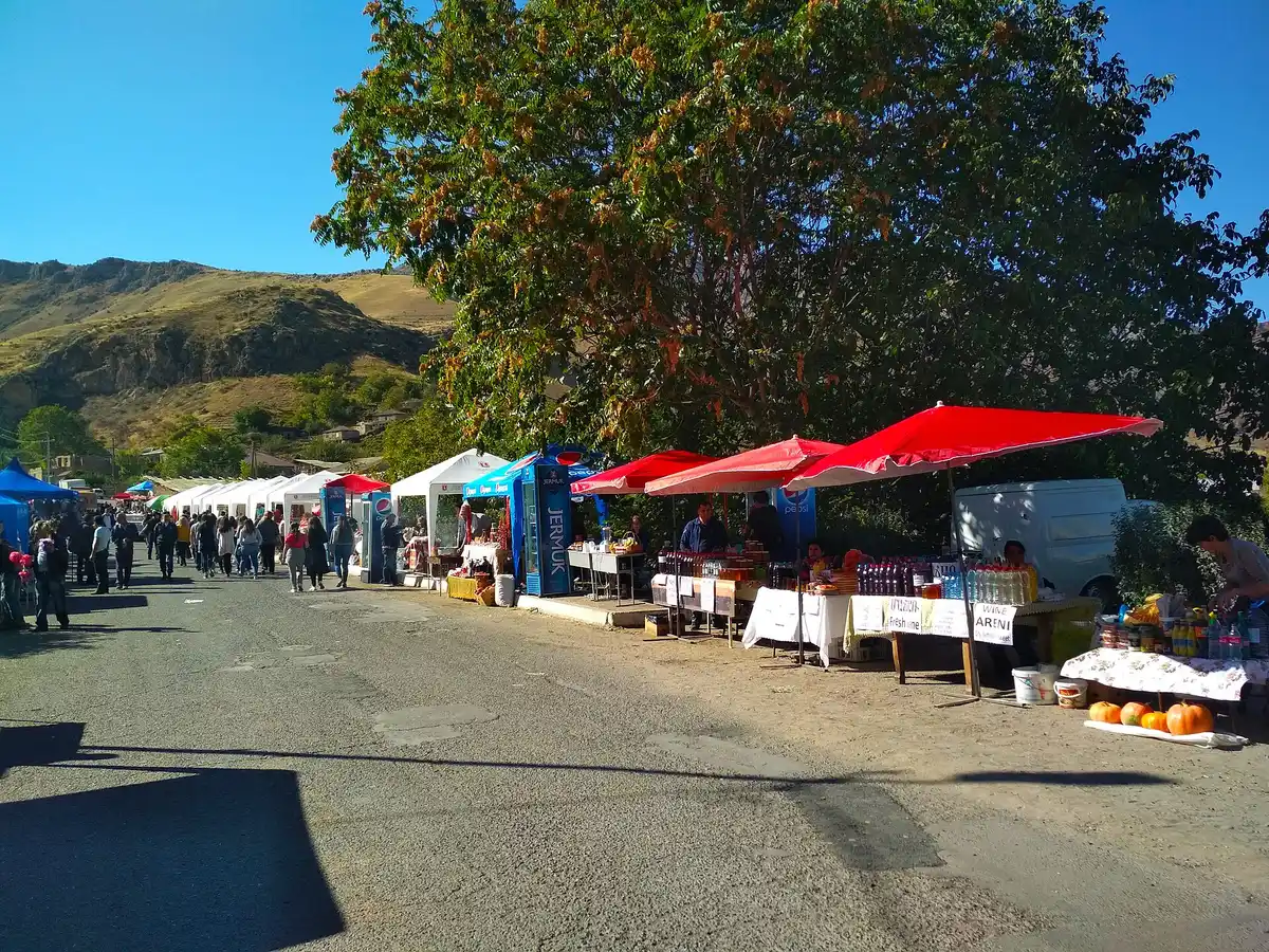 A line of festival stalls and umbrellas along the village road at Areni with bare hills behind