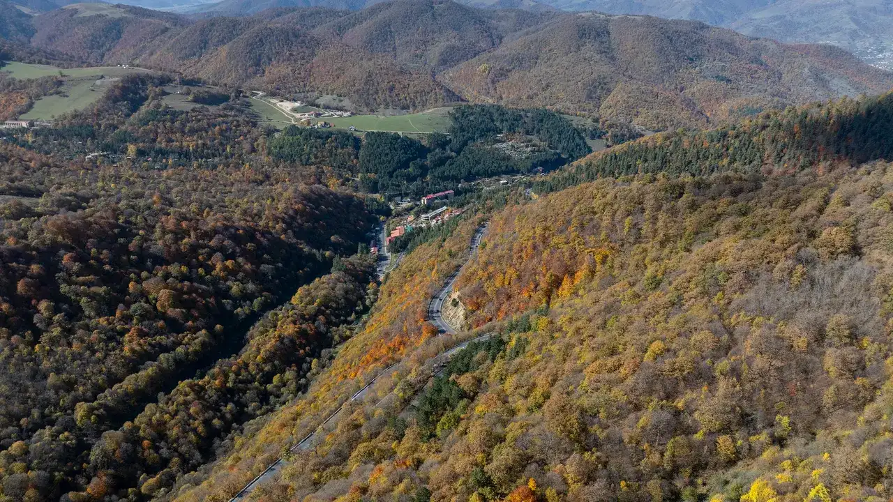 Aerial view of the M4 road curving through orange and gold forest above the Dilijan valley in October