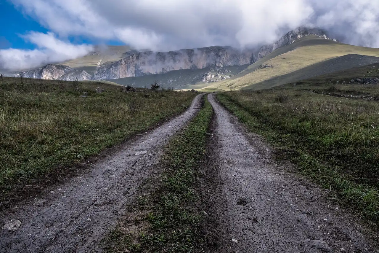A rutted dirt track running towards the cliffs of Mount Dimats under low autumn cloud
