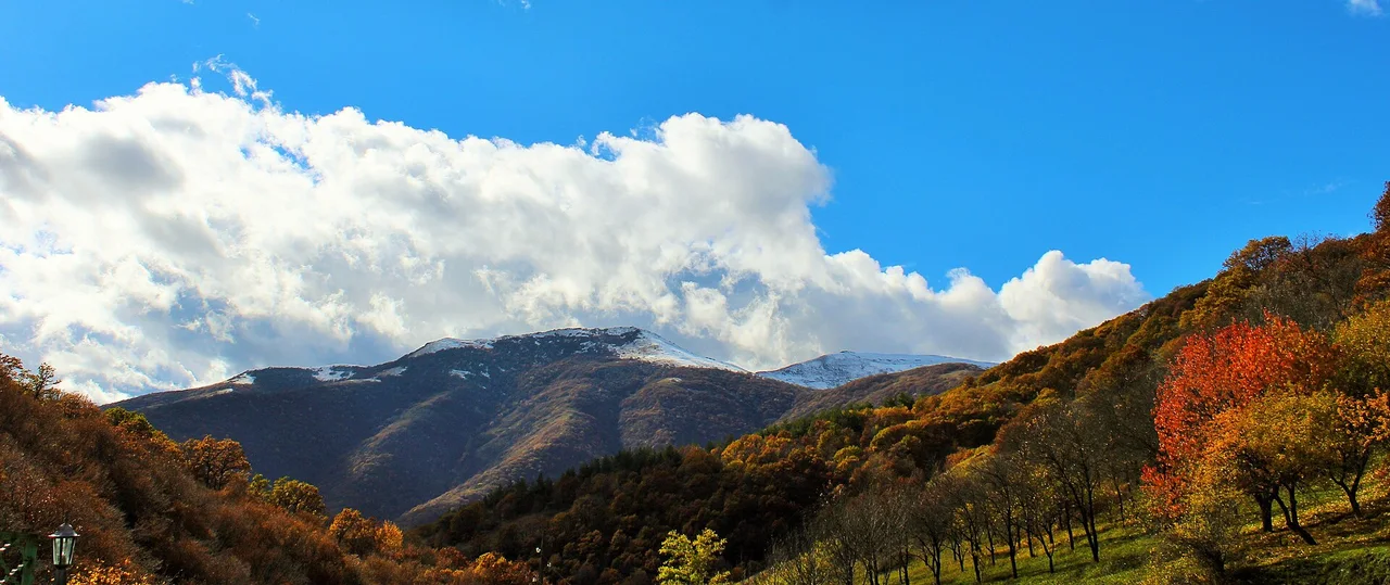 Orange autumn trees in the foreground with the first snow lying on the ridge above Aghveran
