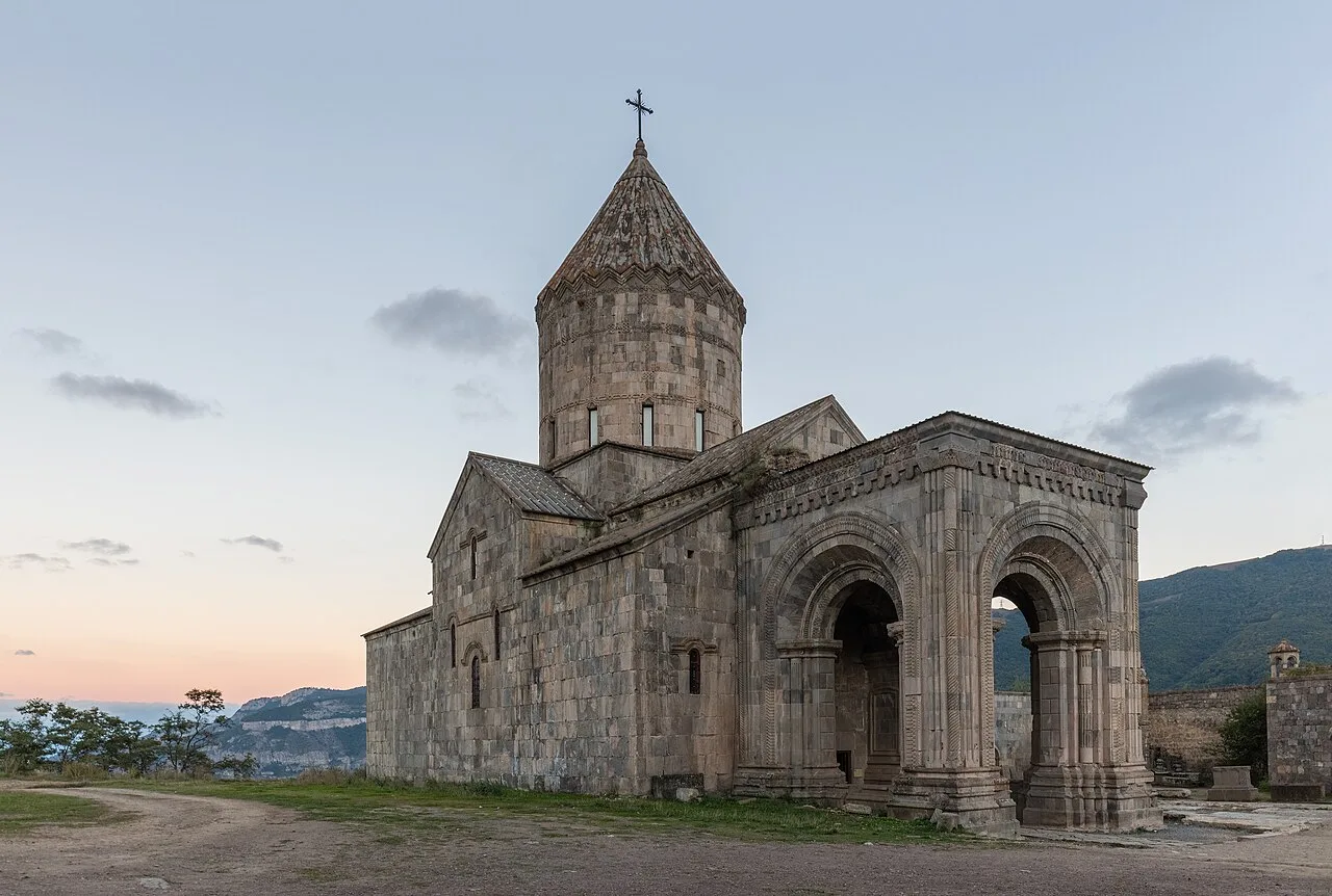 Tatev monastery on its cliff at dusk, with the arched gavit hall and conical dome above the Vorotan gorge