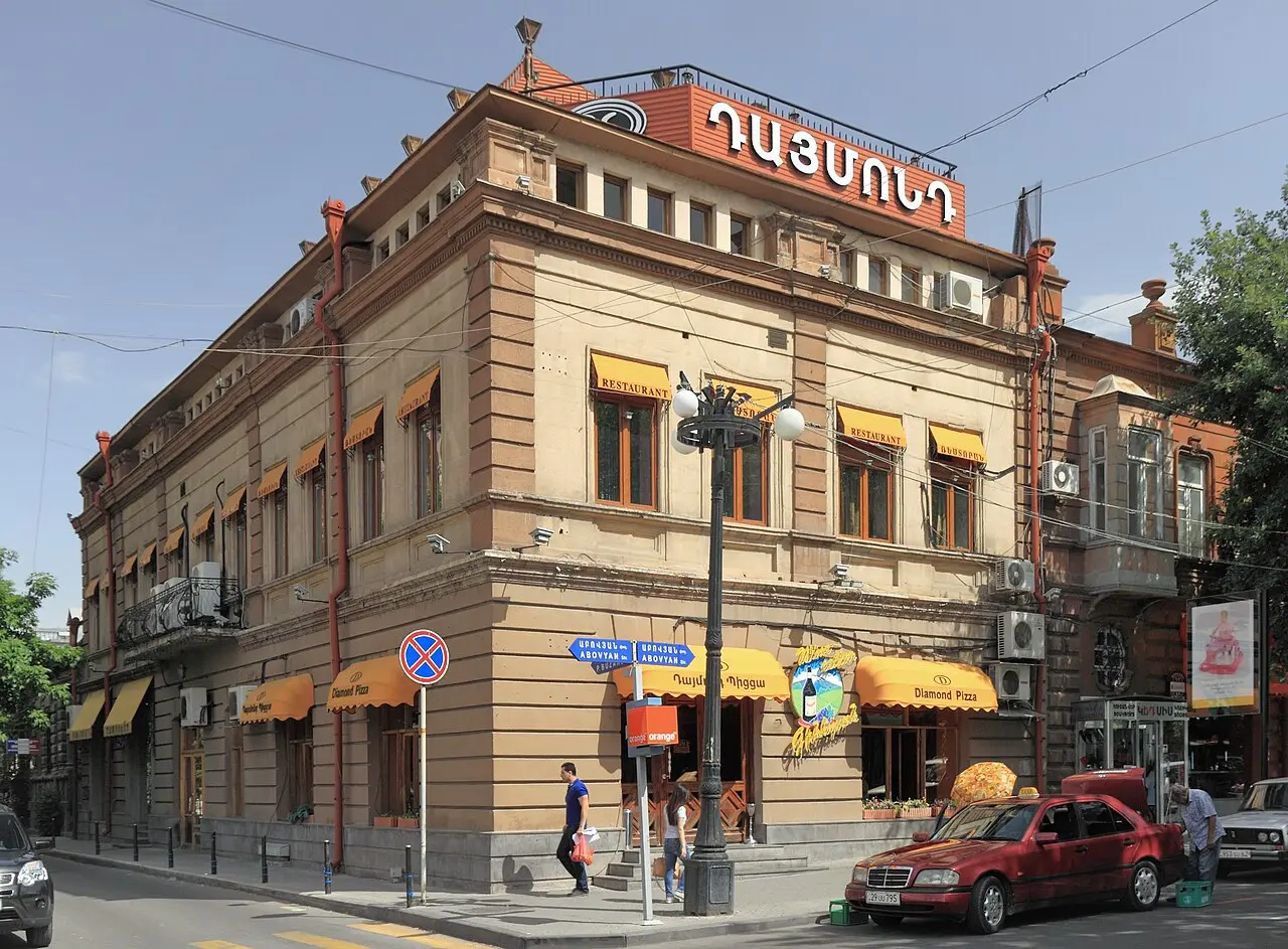 A quiet residential street in central Yerevan lined with balconied tufa buildings and parked cars