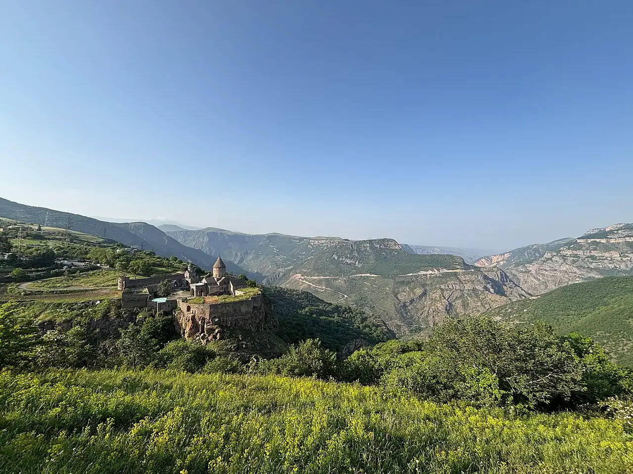 Tatev monastery standing on the edge of a deep green gorge in southern Armenia, with canyon walls and mountains stretching away behind it