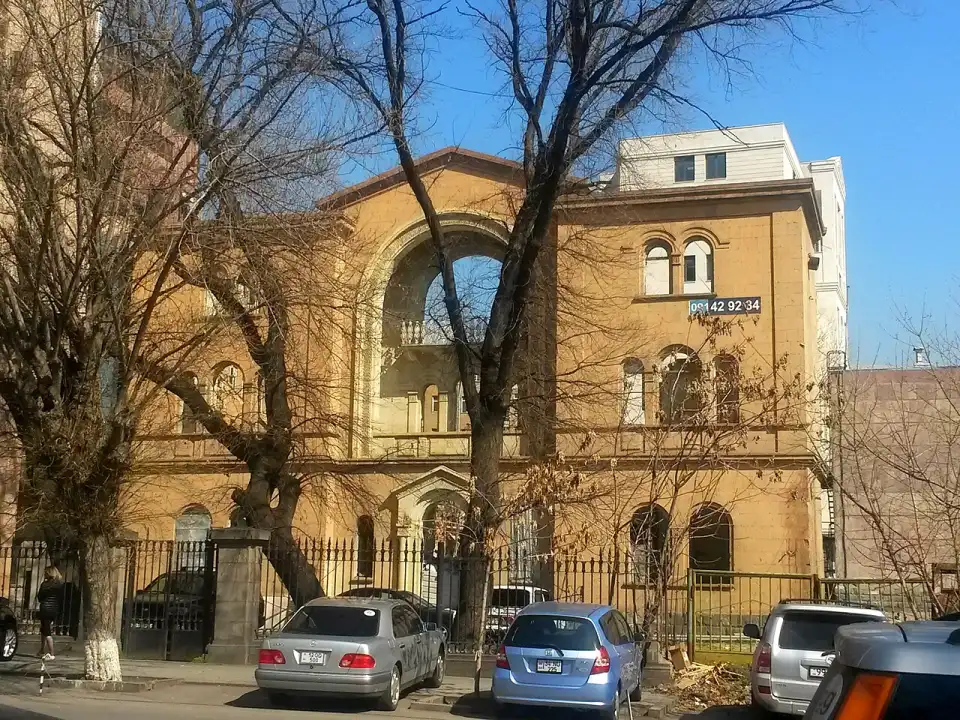 A historic stone government building on a leafy street in central Yerevan