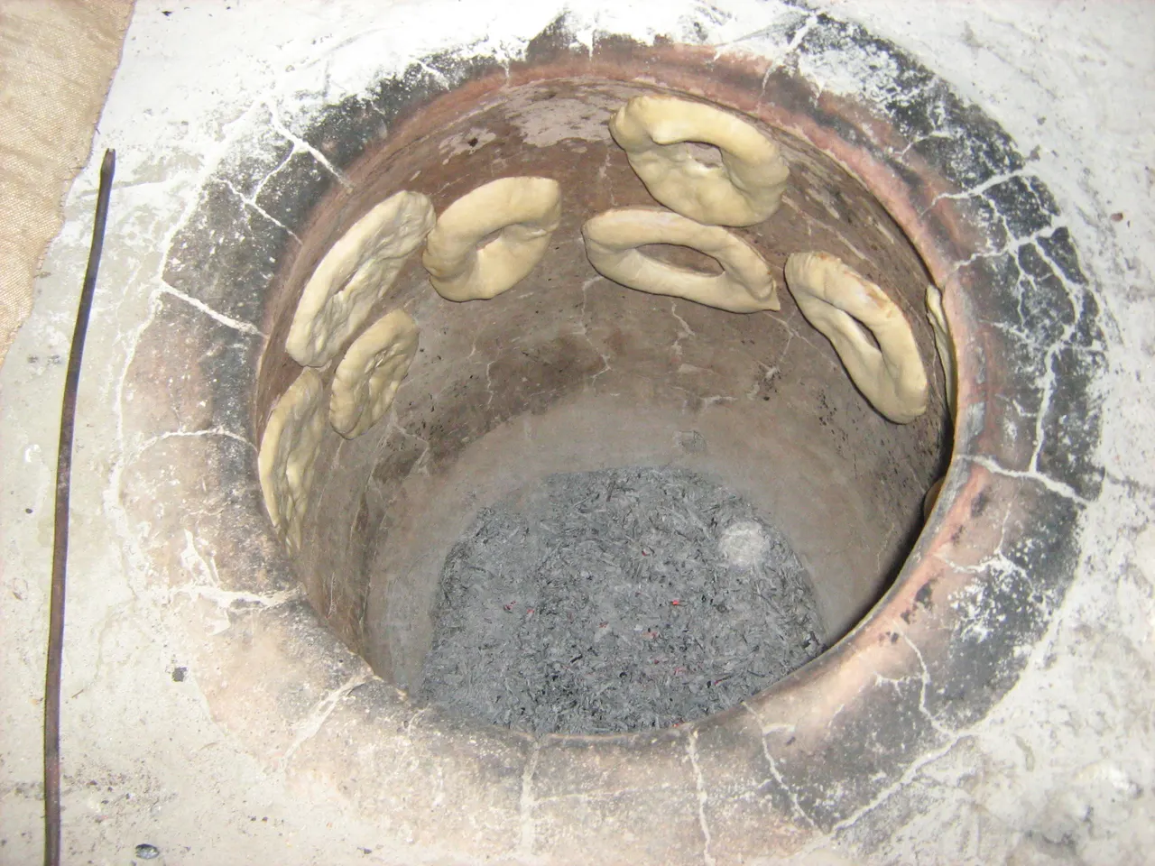 A traditional Armenian tonir, a conical clay oven sunk into the ground, with fire glowing inside