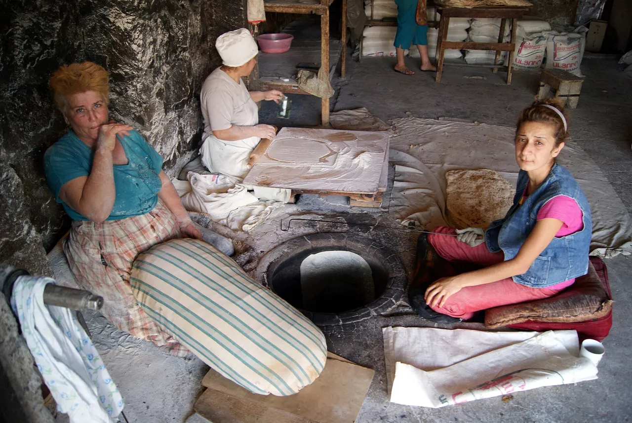 Two Armenian women working together to bake lavash, one stretching dough on a cushion