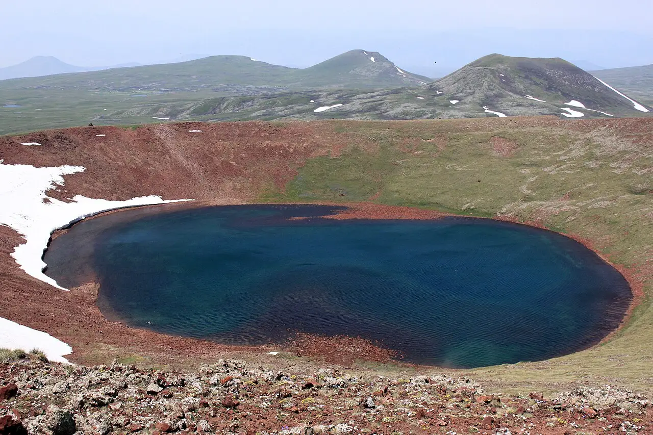 The deep blue crater lake in the red volcanic summit of Mount Azhdahak with the Gegham peaks behind