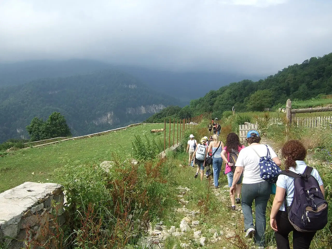 A group of walkers on a stony path along a green ridge above forested valleys in northern Armenia