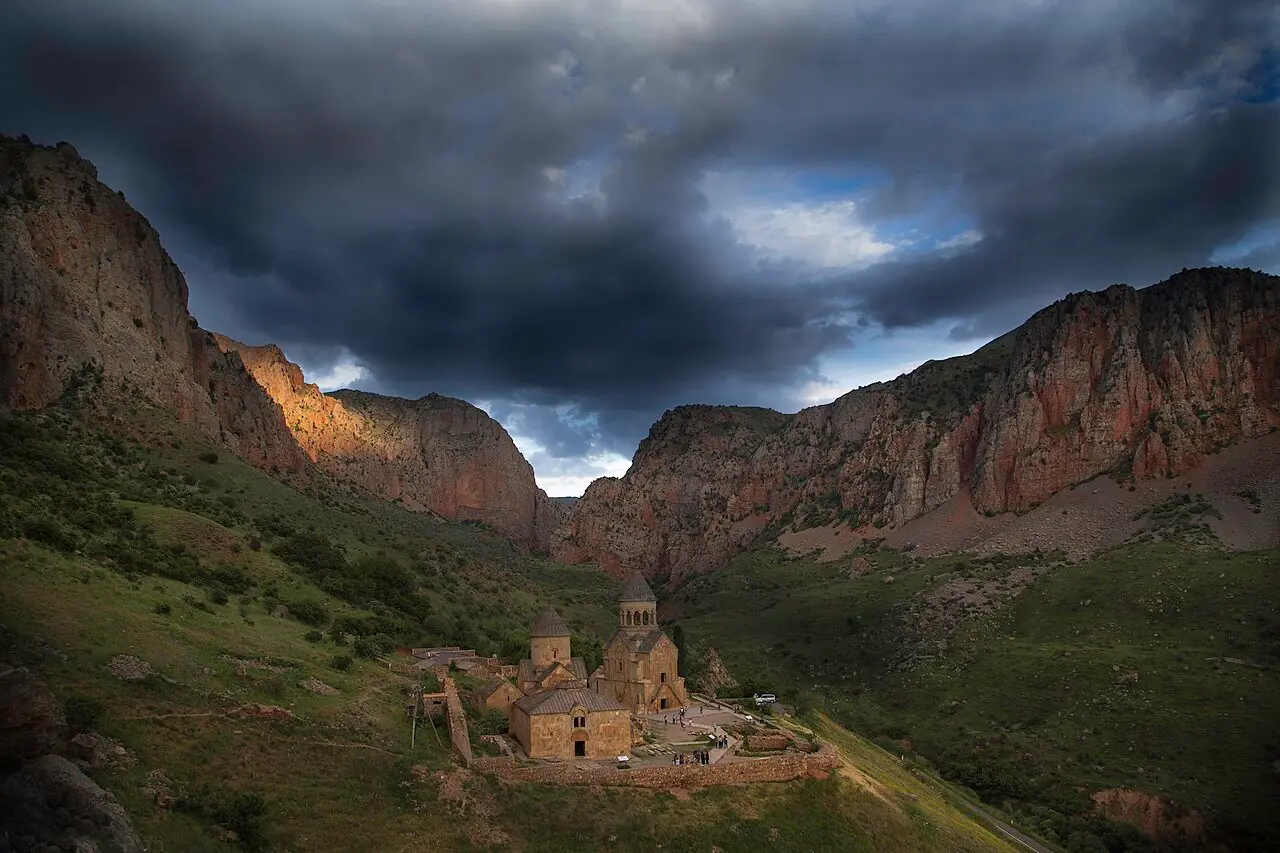 Noravank monastery sitting in the Amaghu canyon under sheer brick-red cliffs and a stormy sky