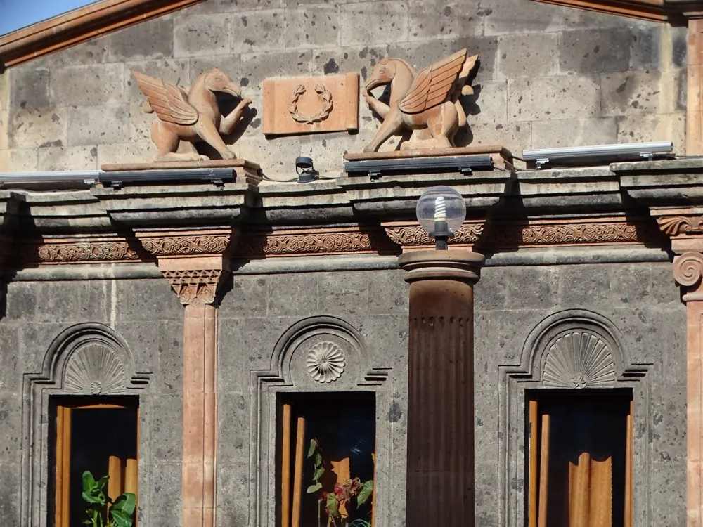 A carved stone facade detail at Poloz Mukuch Beerhouse, with winged horse figures over an arched window in Gyumri black tuff