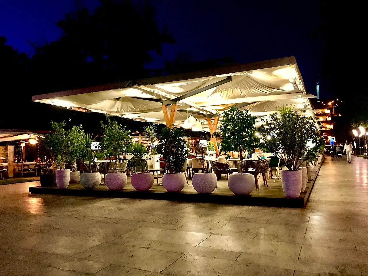 A leafy open-air restaurant terrace on a street in central Yerevan with tables set under trees