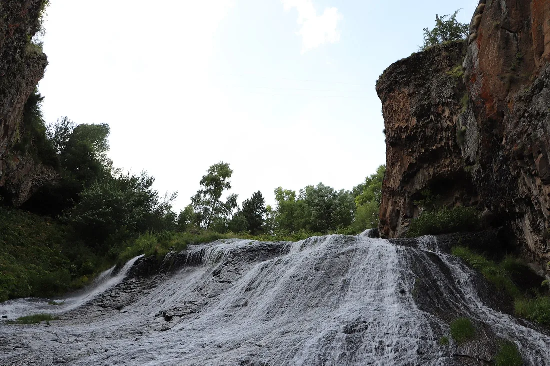The Jermuk waterfall seen from below, water spreading in fine strands down a broad stepped rock face between cliffs