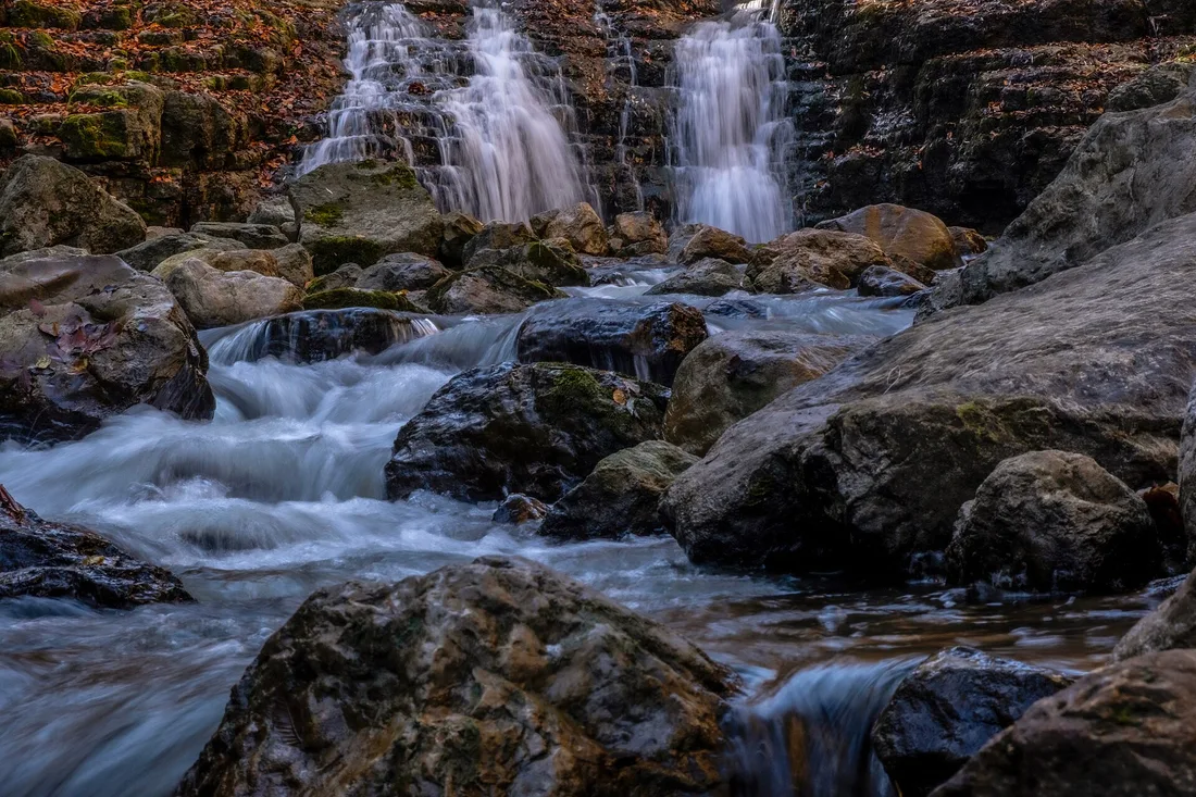 A low stepped waterfall on the Khachaghbyur river running over mossy rocks between autumn leaves in the Lastiver forest