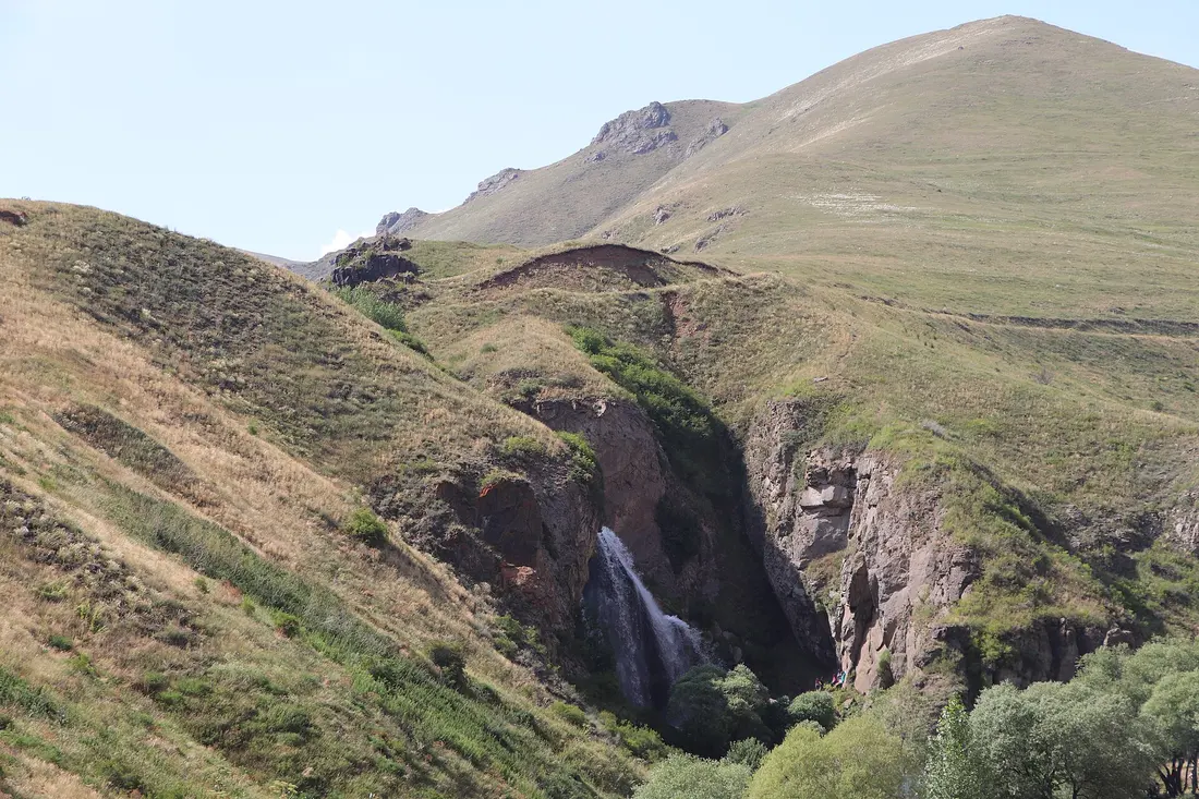Rolling bare hills above the Chichkhan gorge with the Trchkan waterfall barely visible as a thin white line in a fold of red rock