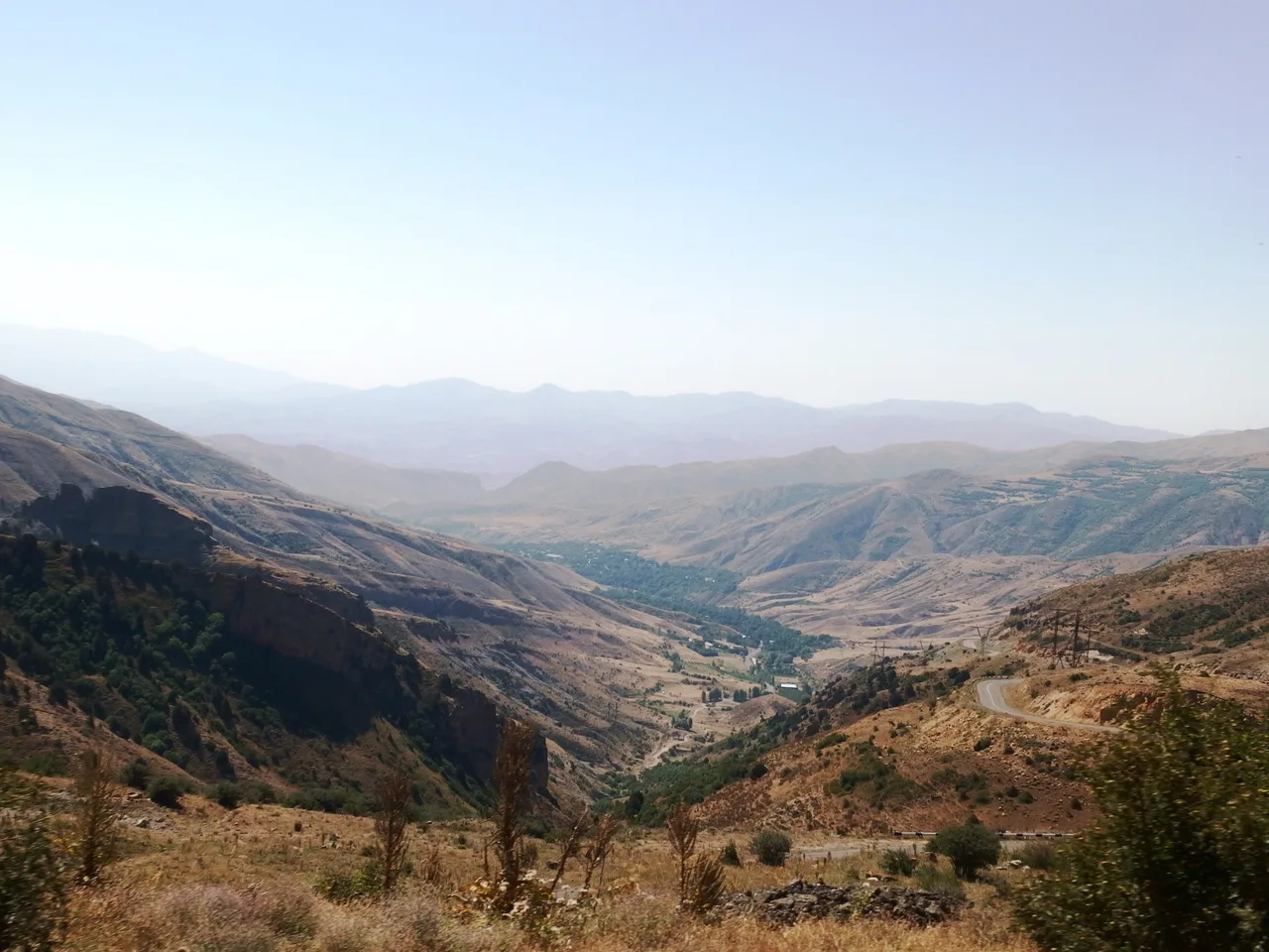 A paved mountain road climbing in tight switchbacks over the grassy Selim pass in southern Armenia under a clear sky