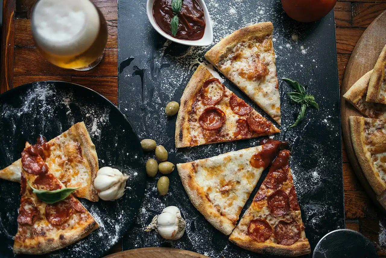 A glass of craft beer next to pizza slices on a rustic wooden table