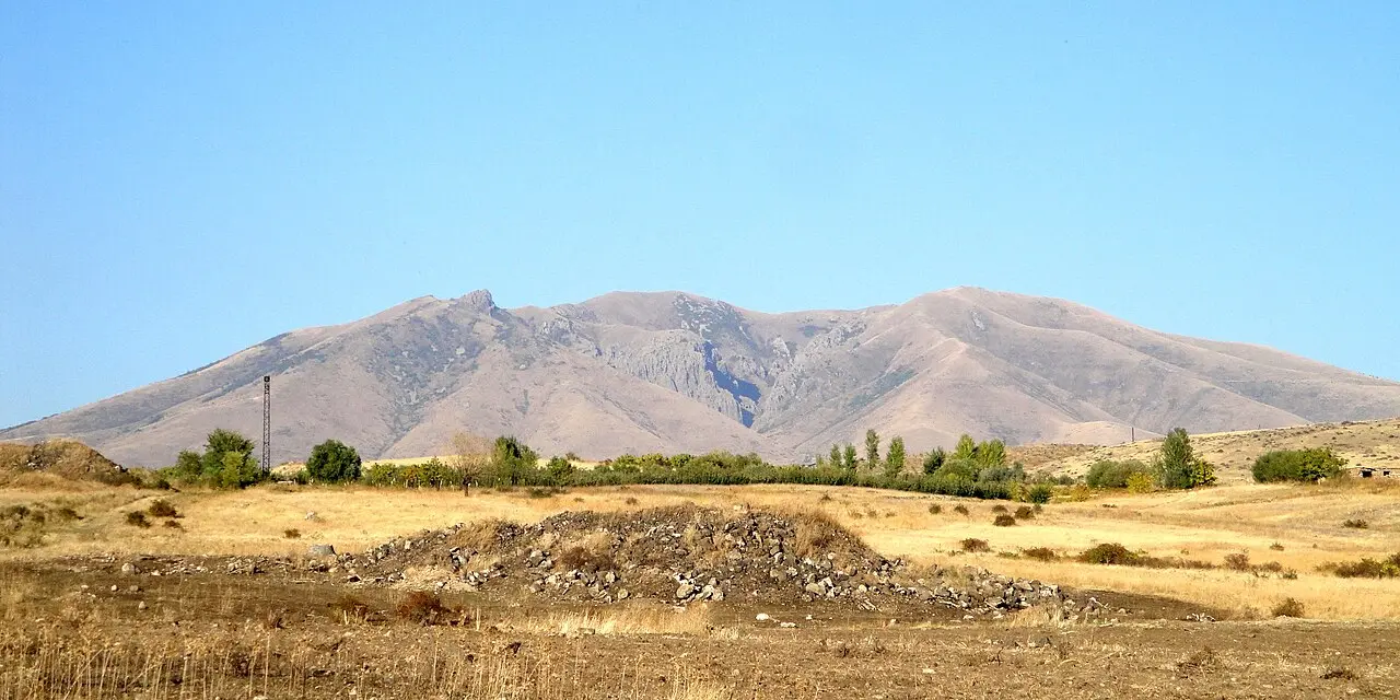 The grassy crater rim of Mount Ara with distant peaks on the horizon