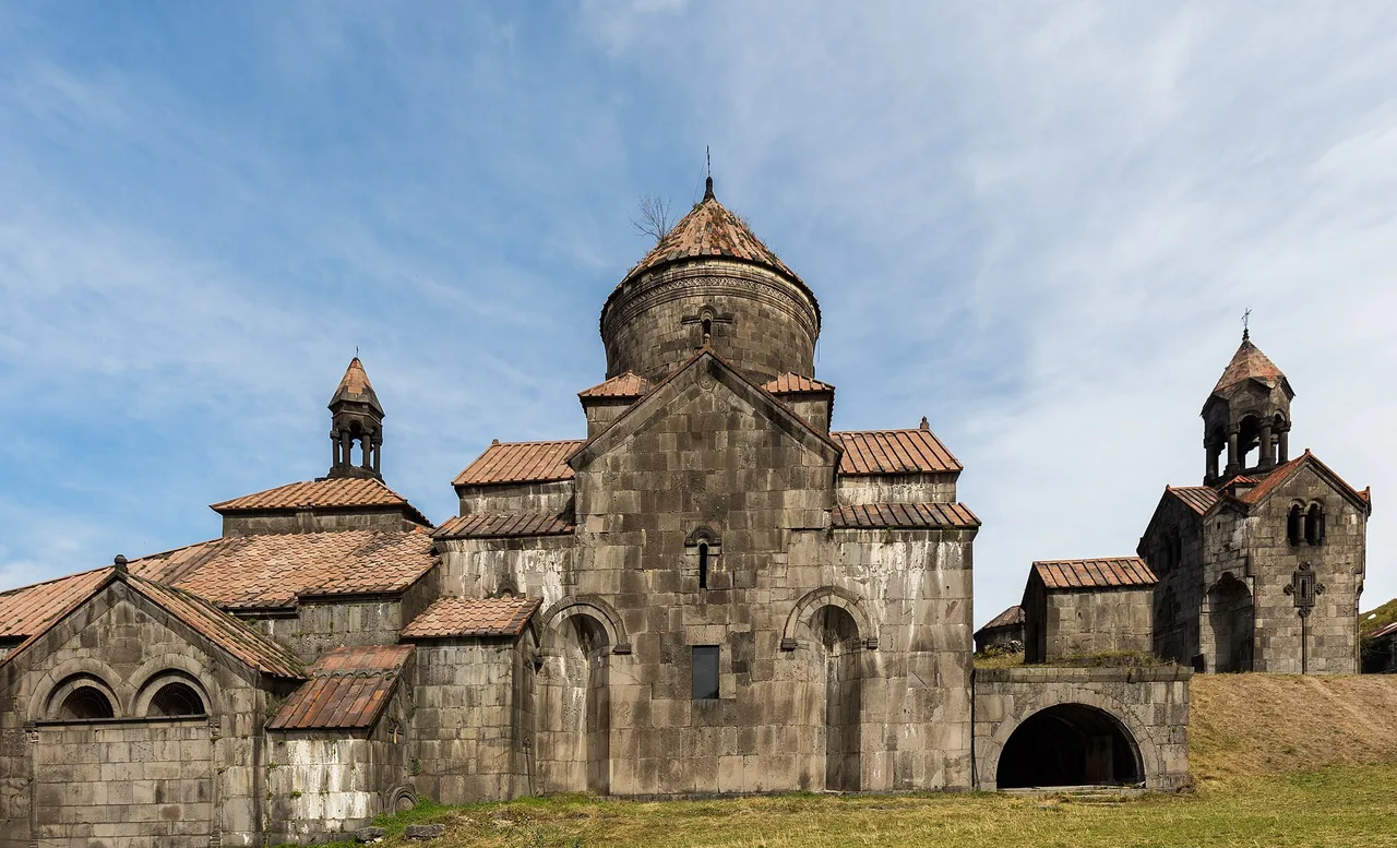 The domes, tiled roofs and belfry of Haghpat monastery standing together on a green shelf under a blue sky