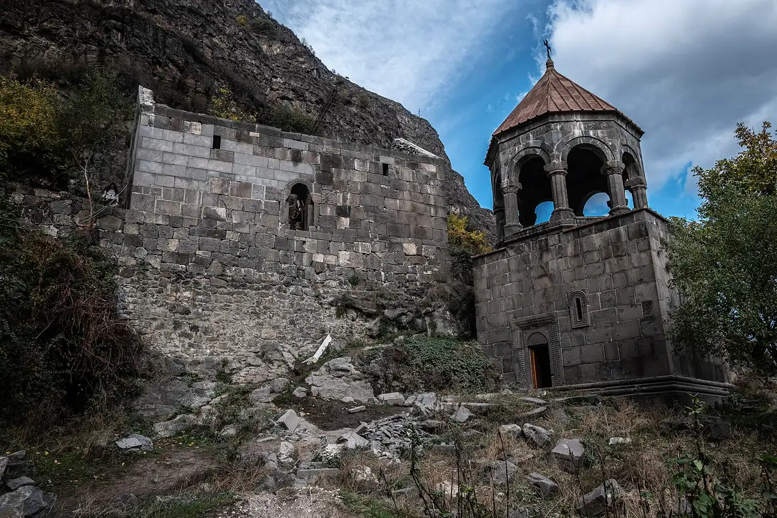 The domed bell tower and broken refectory wall of Kobayr monastery under a dark cliff above the Debed gorge