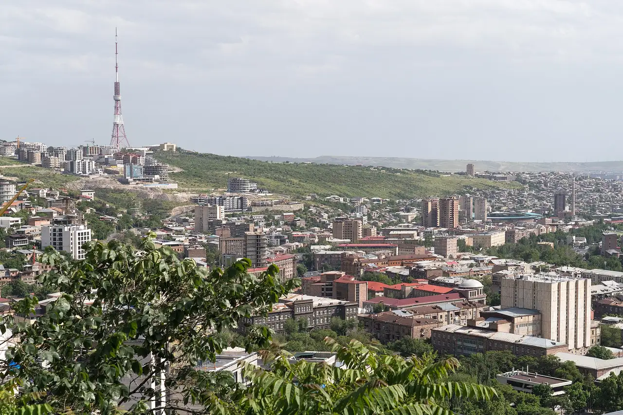 Yerevan spread across its plateau under a pale sky, with the television tower on the ridge and hills closing the far side