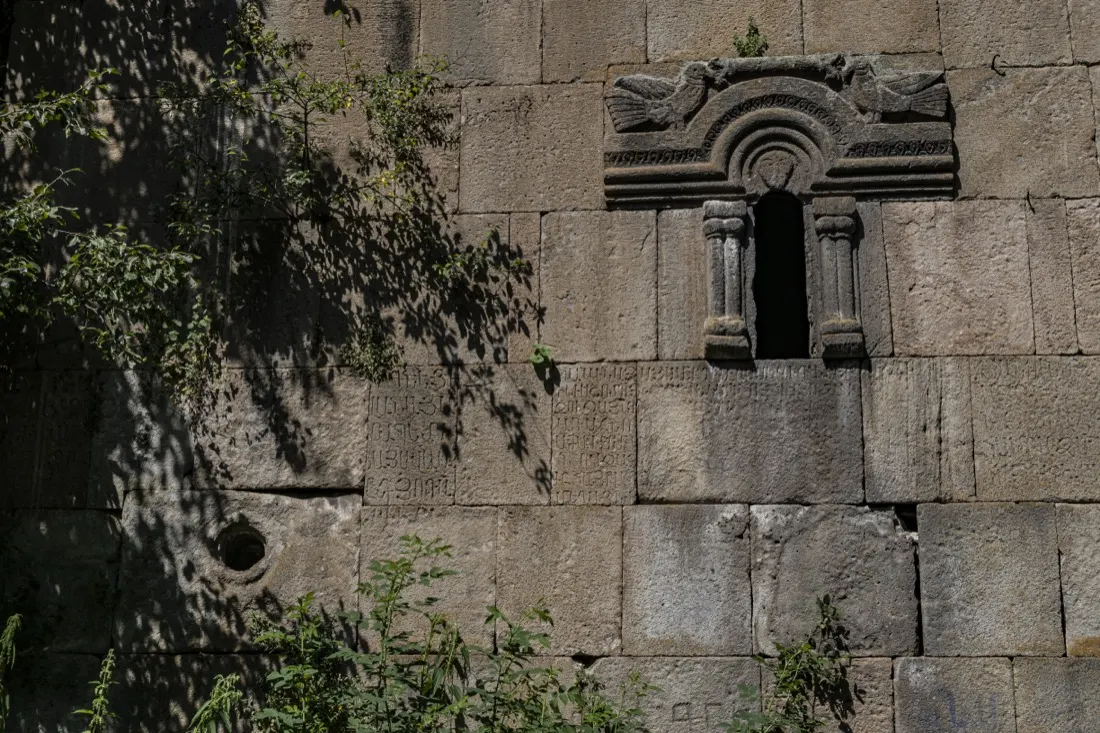 A carved stone window and khachkar detail on the wall of Jukhtak Monastery in Dilijan National Park