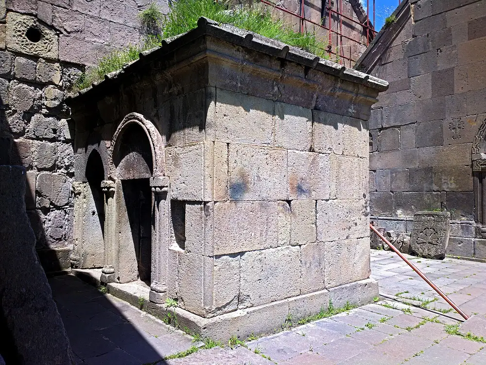 The grey stone churches and bell tower of Goshavank monastery sitting among the houses of Gosh village with wooded hills behind