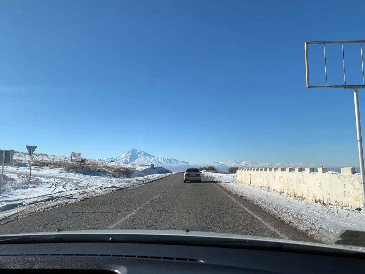 A snow-covered road running through bare hills in Armenia in January under a flat grey sky