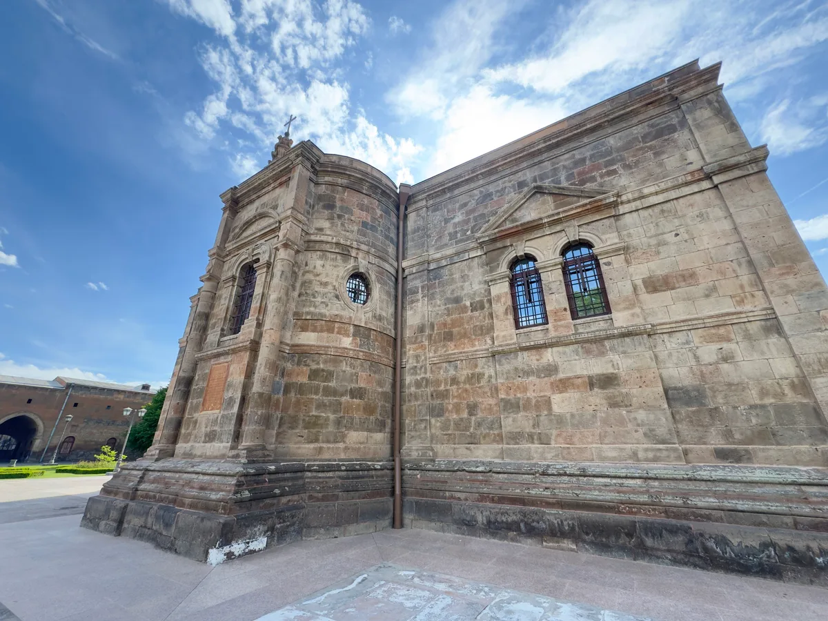 A close view of the carved stonework and belfry of Etchmiadzin Cathedral against a blue sky
