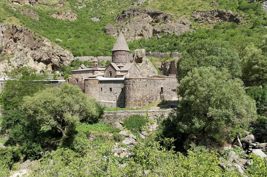 Geghard monastery, its domed church and fortified walls set in the green Azat river gorge with cliffs rising behind it