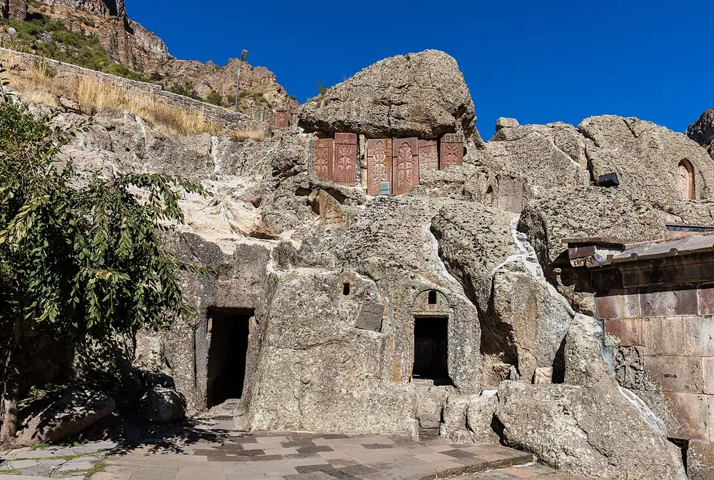 Rows of carved khachkars and rock-cut chapel doorways hewn directly into the tuff cliff face at Geghard monastery