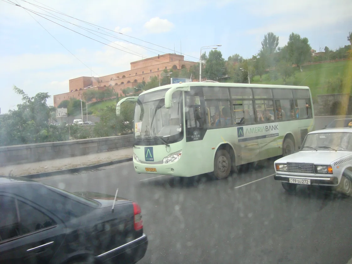 A city bus on a busy street in central Yerevan with passengers waiting at the stop