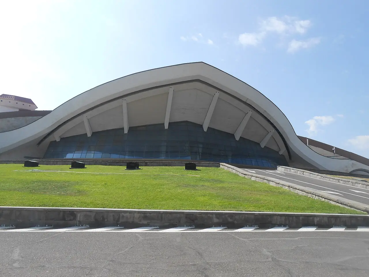 The sweeping modernist roof of the Karen Demirchyan Sports and Concerts Complex above green lawns in Yerevan
