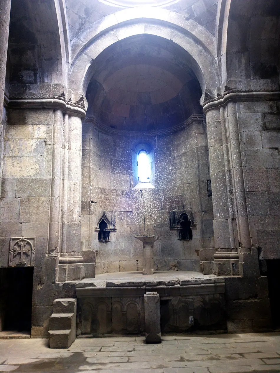 Domed stone interior of a church at Goshavank, a single narrow window lighting the apse and a carved khachkar set into the pier at left