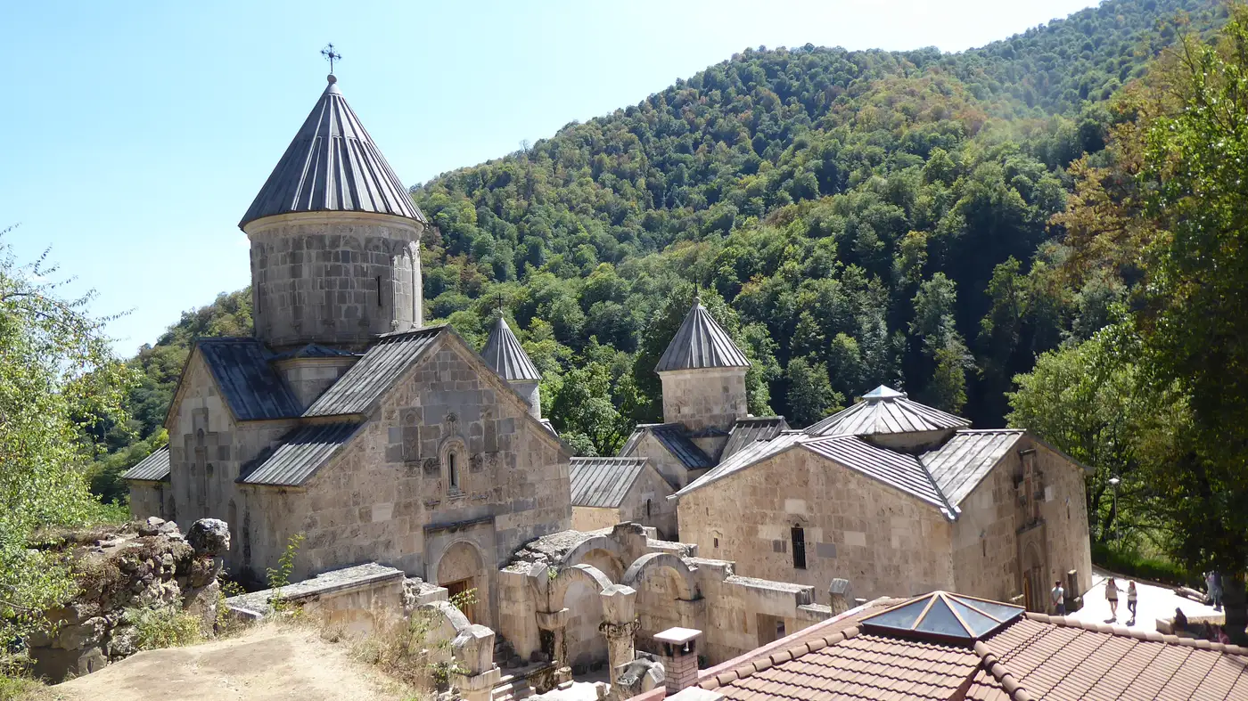 An elevated view of the conical domes and stone roofs of the Haghartsin complex against a forested hillside