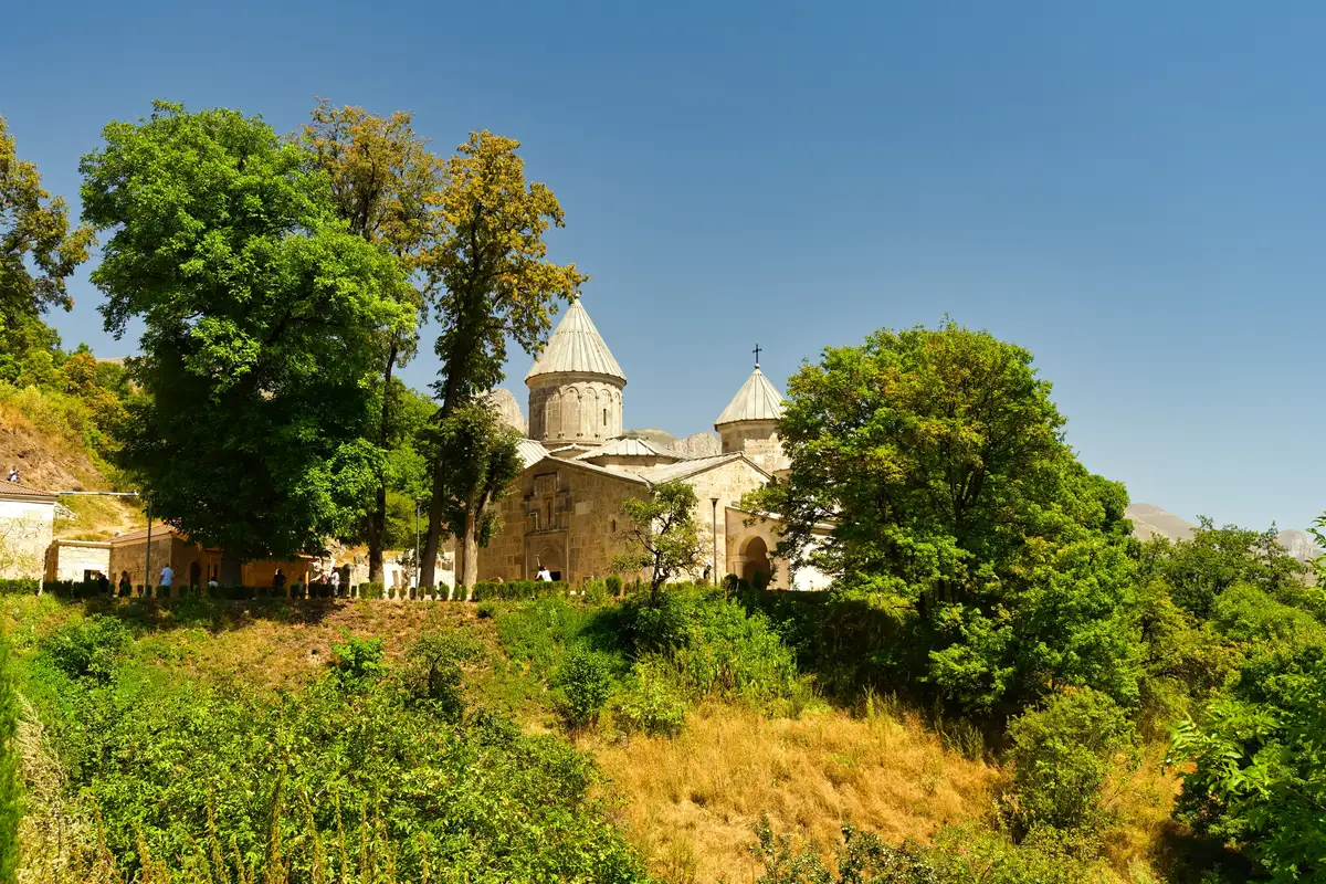 The stone church of Haghartsin with its conical dome rising above green trees on a summer day