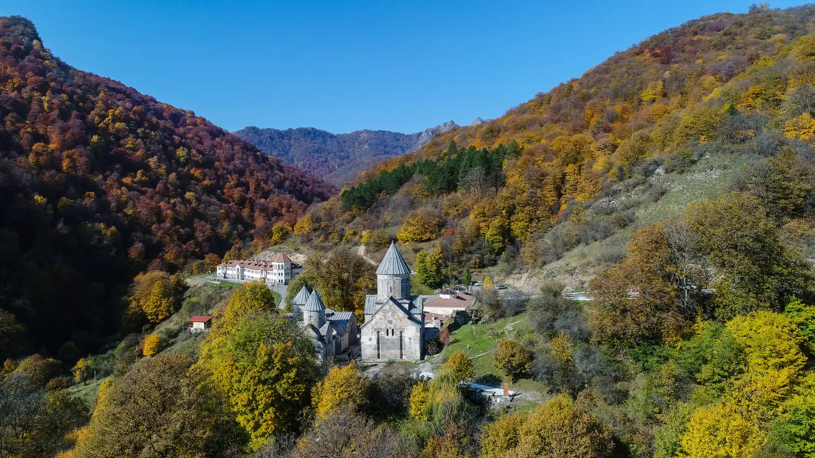 Aerial view of Haghartsin monastery in a forest clearing surrounded by autumn-coloured wooded hills above Dilijan