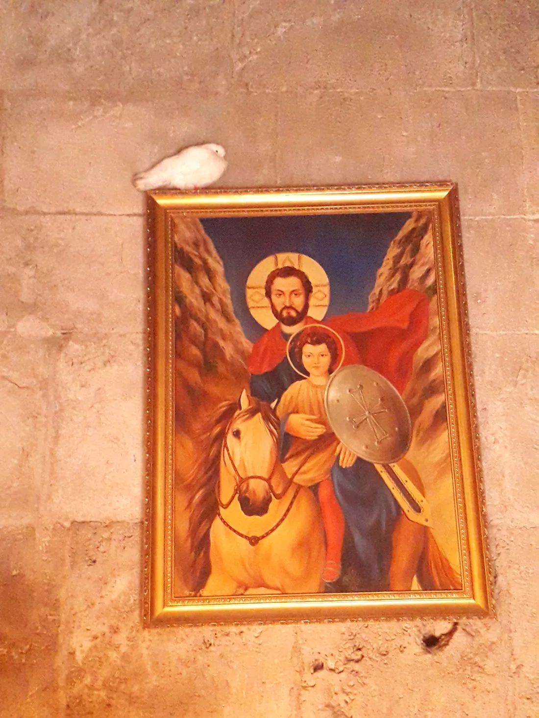 A white dove perched beside a framed devotional icon on a stone wall inside Haghartsin monastery
