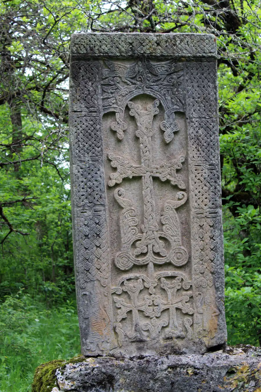 A finely carved Armenian khachkar cross-stone with interlace ornament standing among trees at Haghartsin